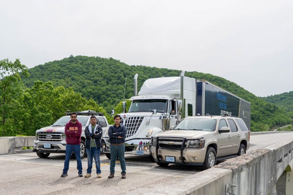 Three people in front of vehicles on a bridge