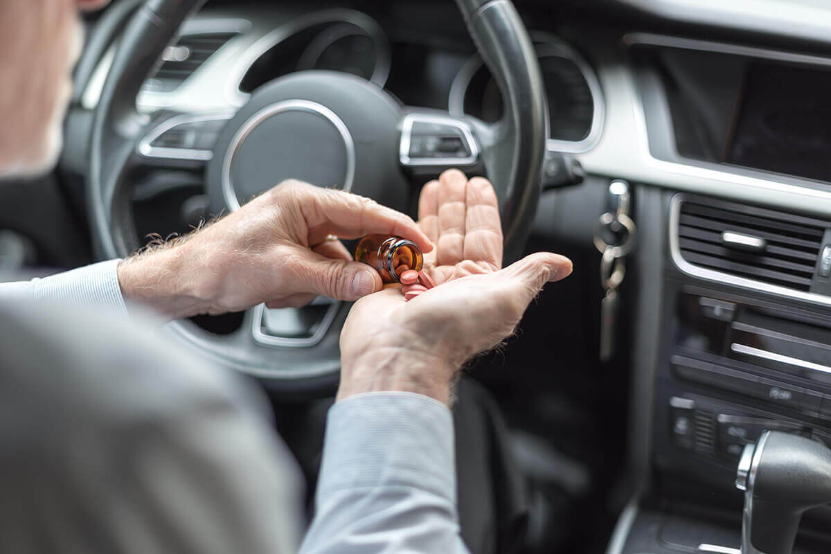 A person holding pills while sitting on the driver's side of a vehicle